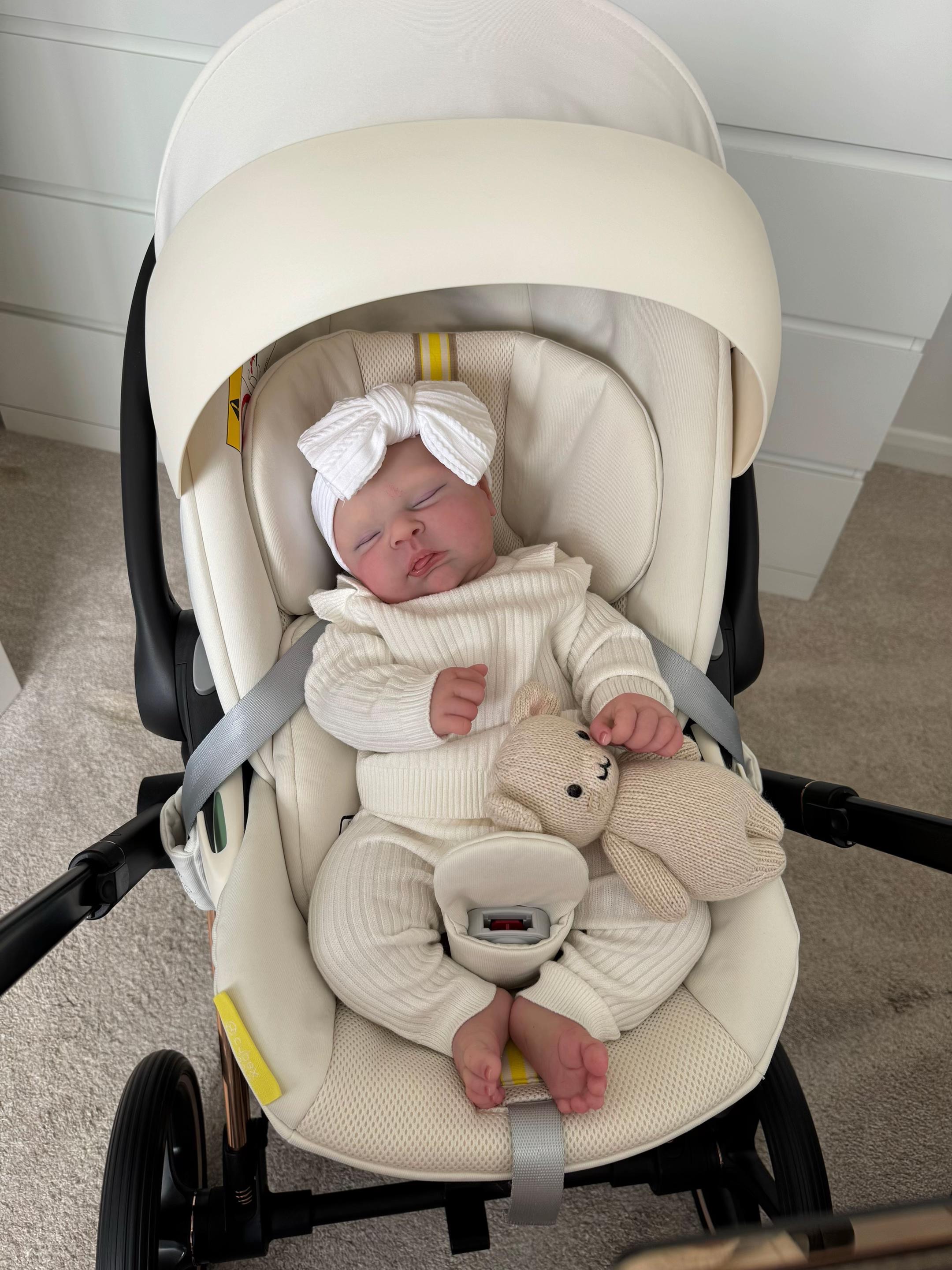 Baby Lena Bald Edition, an 18.5-inch realistic chubby full body silicone newborn baby girl doll sleeping in a cream bouncer in a blue dress by Reborn Heaven.